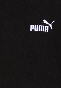 Melns kokvilnas T-krekls ar baltu izšūtu Puma logotipu un lecošu siluetu, izvietots uz teksturētas auduma fona.