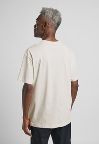 T-shirt in cotone beige chiaro con maniche corte e collo rotondo, caratterizzata da una vestibilità comoda e un tessuto liscio, senza texture.