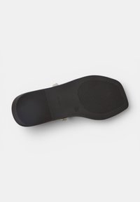 Suela negra plana de sandalia con agarre texturizado y un pequeño tacón, vista desde abajo sobre un fondo blanco.