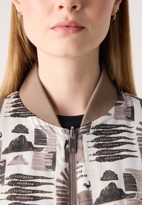 Giubbotto bomber con un colletto a coste beige-marrone, caratterizzato da un design astratto stampato in toni tenui, zip argentata e una trama di tessuto soffice.