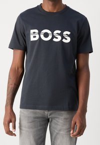 Mörkblå bomulls t-shirt med en stor vit "BOSS" logotyp över bröstet. Korta ärmar, rund halsringning och avslappnad passform.