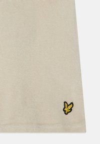 Beiger Stoff mit einer weichen Textur, der in der unteren rechten Ecke ein kleines, buntes gesticktes Logo eines Vogels zeigt.