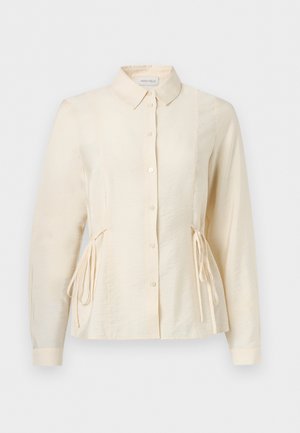 Bluza dugih rukava krem boje s gumbima sprijeda, ovratnikom i podesivim bočnim vezicama za prianjanje u struku.