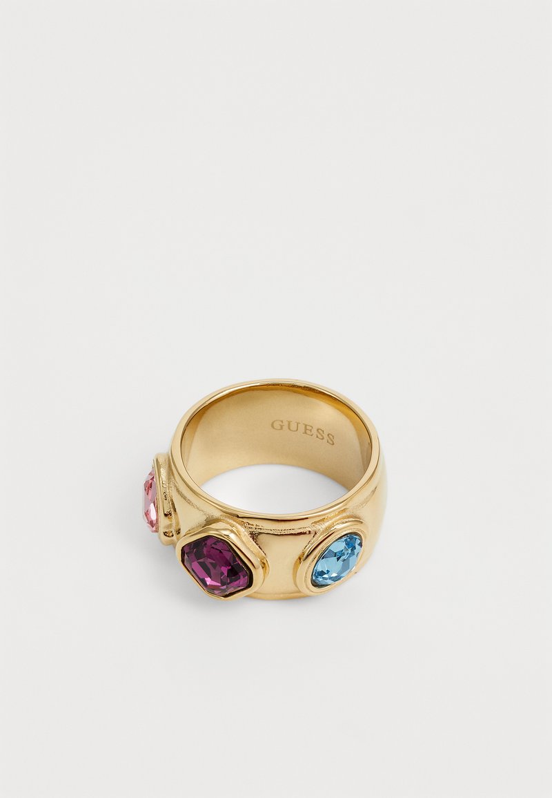 Guldmetalring med tre sekskantede ædelstene: pink, lilla og blå. Indersiden er gravet med brandnavnet "GUESS."