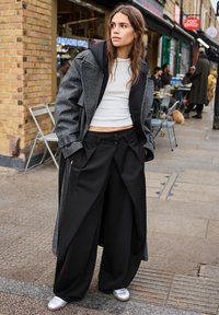 Gray, oversized coat with a black hood, white crop top, and wide black trousers paired with shiny silver shoes on a street setting.