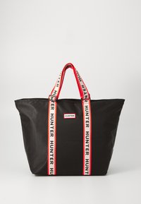 Bolsa tote negra hecha de nailon duradero, con asas de marca en rojo y blanco y un parche rectangular con el logotipo en la parte delantera.