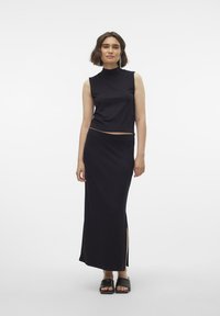 Svart ermeløs topp og lang skjørt, med sideslisser. Glatt stoff med en tettsittende design. Brukt med svarte åpne sandaler.