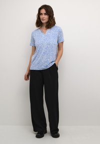 Camiseta de manga corta azul con un patrón blanco texturizado, con escote en V. Combinada con pantalones anchos negros y zapatos negros.