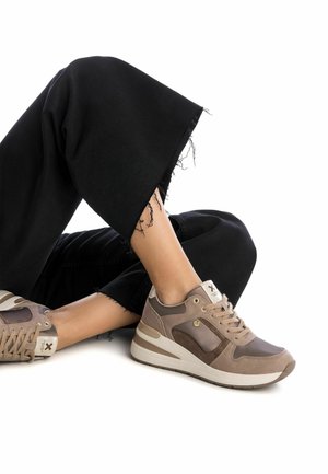 Baskets marron avec un mélange de matériaux lisses et texturés, dotées de lacets, d'accents dorés et d'une semelle rembourrée. Pantalons noirs avec un ourlet effiloché.