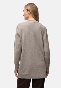 Ljusgrå tröja med löst snitt, ribbade ärmslut och rak fåll. Mjuk textur och rundad halsringning, med ett subtilt stickat mönster.