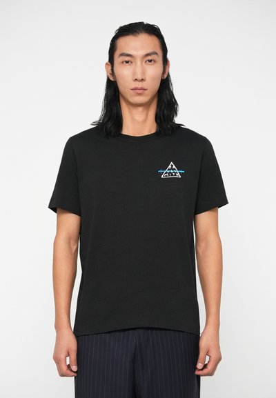 Juodas medvilnės marškinėliai trumpomis rankovėmis, apvaliu kaklu ir maža trikampė išsiuvinėta etikete balta ir mėlyna spalvomis ant krūtinės.