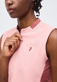 Άτομο που φοράει αμάνικη ροζ ποδηλατική φανέλα με φερμουάρ στο γιακά τραβά λίγο το φερμουάρ προς τα κάτω.