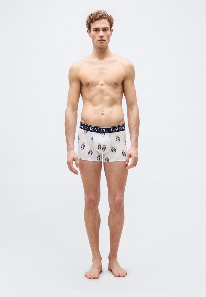 Νέος άνδρας στέκεται ξυπόλυτος, φορώντας λευκά μπόξερ με στάμπες αρκουδάκια και μπλε σκούρο λάστιχο μέσης με την ετικέτα "Polo Ralph Lauren".