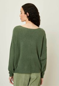 Grøn strikket sweater med en bred bådudskæring, drop skuldre og ribbede manchetter, der har en blød tekstur og en afslappet pasform.