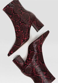 Bottes cheville à imprimé serpent rouge et noir avec fermeture éclair, bout pointu et talon épais. Matière texturée avec une finition brillante.
