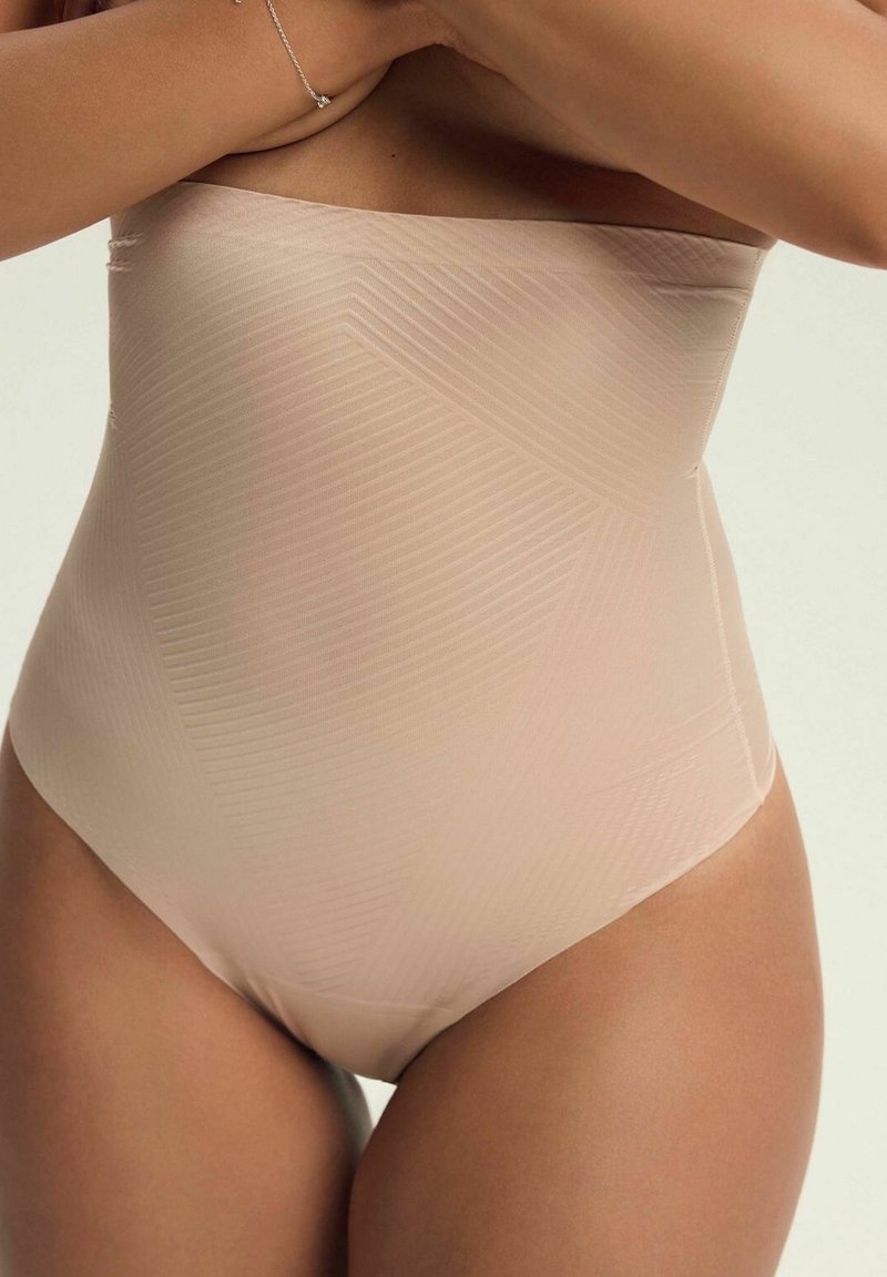 Beżowy bodysuit bez ramiączek o prążkowanej fakturze, z wysokim stanem i gładką powierzchnią, zdobiony delikatnymi skośnymi wzorami na tkaninie.