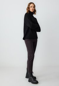 Zwarte gebreide coltrui met een ontspannen pasvorm en geribbelde zoom, gecombineerd met donkerpaarse slim-fit broek en zwarte veterschoenen met een enkellange schacht.