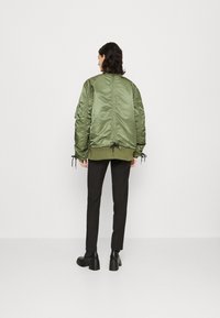 Olive green bomber jacket with a satin finish, featuring a knit hem and cuffs, adjustable drawstrings, and a streamlined silhouette.