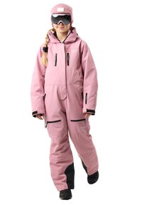 Tuta da neve rosa con tessuto impermeabile, numerose tasche con cerniera, dettagli neri su polsini e gambe, e un cappello e occhiali abbinati in rosa.