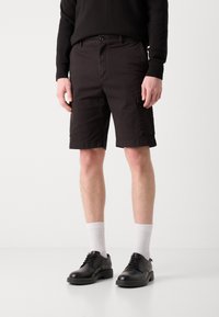 Svarte cargo-shorts har en rett snitt, med en sidelomme, laget av slitesterkt stoff. Kombinert med hvite sokker og svarte snøremotorsykler.