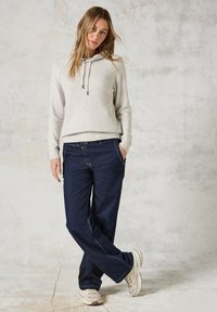 Lichtgrijze geribde trui met een capuchon en aantrekkoord, gecombineerd met donkerblauwe wijde jeans. Witte sneakers maken de outfit compleet.
