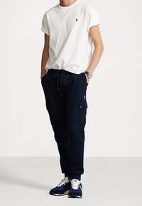 Vit bomull t-shirt med rullade ärmar och mörkblå träningsoverallsbyxor med cargofickor. Svarta och blå sneakers med vita snören fulländar looken.