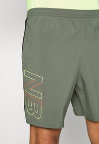 Khaki sportovní šortky z lehké tkaniny s černým bočním panelem a velkým logem "NB" žluté a červené barvy na levé noze.