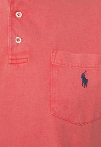 Korálové polo tričko vyrobené z bavlny, s pěticí tlačítek, levým kapsičkovým designem a tmavě modro vyšitým logem koně a jezdce.