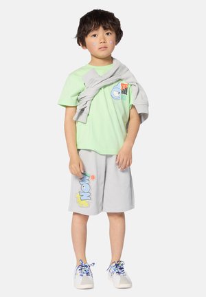 Green short-sleeve t-shirt with graphic, gray shorts with "WOW" print, gray sweatshirt draped, multicolored sneakers with blue laces.