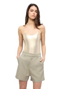 Camisole metallico dorato con spalline sottili abbinato a pantaloni corti beige chiaro su misura con tasche laterali e vestibilità rilassata.