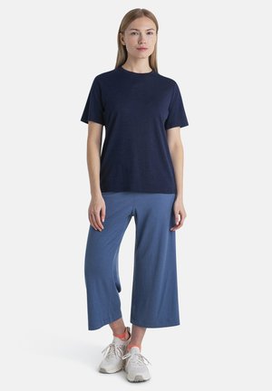 Navy crew-neck t-shirt paired with blue wide-legged pants, featuring a soft texture and relaxed fit, completed with white and orange sneakers.