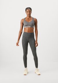 Sivi sportski grudnjak s Nike logotip trakom; crne tajice visokog struka s zavojitim uzorkom; uparene s laganim tenisicama.