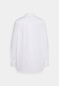 Chemise blanche à manches longues avec col, vue de dos sur un fond clair uni.