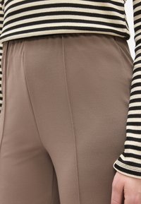 Calças castanhas elásticas com uma textura suave, combinadas com um top às riscas preto e branco. O conjunto apresenta um cós elástico confortável.