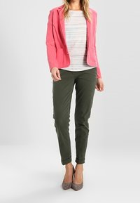 Blazer rose côtelé, chemise rayée, pantalon vert et talons gris. La tenue se caractérise par une coupe ajustée, un pantalon à revers et des accessoires minimalistes.