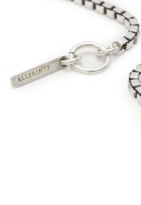 Collana in metallo tono argento con design a catena piatta, dotata di un'etichetta incisa con "ALLSAINTS" e un dettaglio a chiusura circolare.