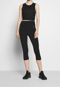 Ensemble de vêtements de sport noir comprenant un débardeur court texturé et un legging capri ajusté. Les deux articles sont en matériau lisse et extensible.