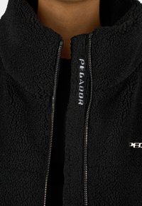 Giacca in fleece nera con colletto alto, caratterizzata da una chiusura con zip e ricamo "Pecador" sulla parte anteriore. Tessuto morbido e testurizzato.