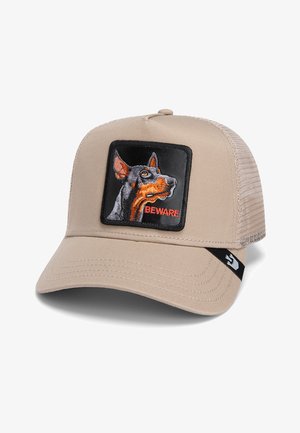 Gorra beige con malla en la parte posterior; presenta un parche cuadrado negro con un perro bordado y el texto "CUIDADO" en rojo. Visera estructurada con detalles de costura.