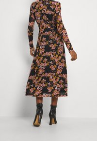 Blommig midiklänning i svart tyg med långa ärmar och en figursydd midja. Designen visar rosa och gula blommönster mot bakgrunden.