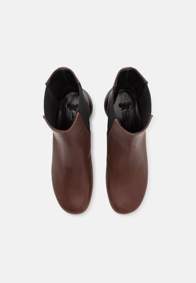 Bottines en cuir marron avec une finition lisse, des côtés élastiques et des talons arrondis. L'intérieur présente une doublure noire avec un détail de logo discret.