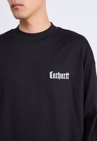 Čierne tričko s dlhým rukávom vyrobené z bavlny, s okrúhlym výstrihom. Na hrudi sa nachádza biele logo s textom "Carhartt". Hladká textura.