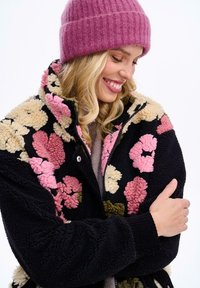 Fleecová bunda s květinovými vzory v růžové, krémové a olivově zelené na černém pozadí; měkká textura, vysoký límec a zip vpředu.