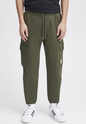 Olive green cargo pants with an elastic waistband, side pockets, and tapered legs, paired with white sneakers featuring black stripes.