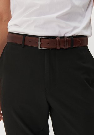 Cinturón de cuero marrón con un acabado texturizado, hebilla de plata y dos bucles ajustables, llevado sobre pantalones negros y una camisa blanca.