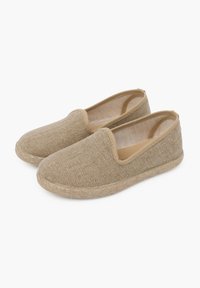 Zapatos beiges sin cordones hechos de tela texturizada con una suela de yute trenzado. Punta redondeada, lados bajos y sin hardware visible ni adornos.