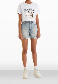 Camiseta blanca con personajes de dibujos animados y el texto "¡Eso es todo, amigos!" combinada con pantalones cortos de mezclilla desgastados en azul claro y zapatillas blancas.