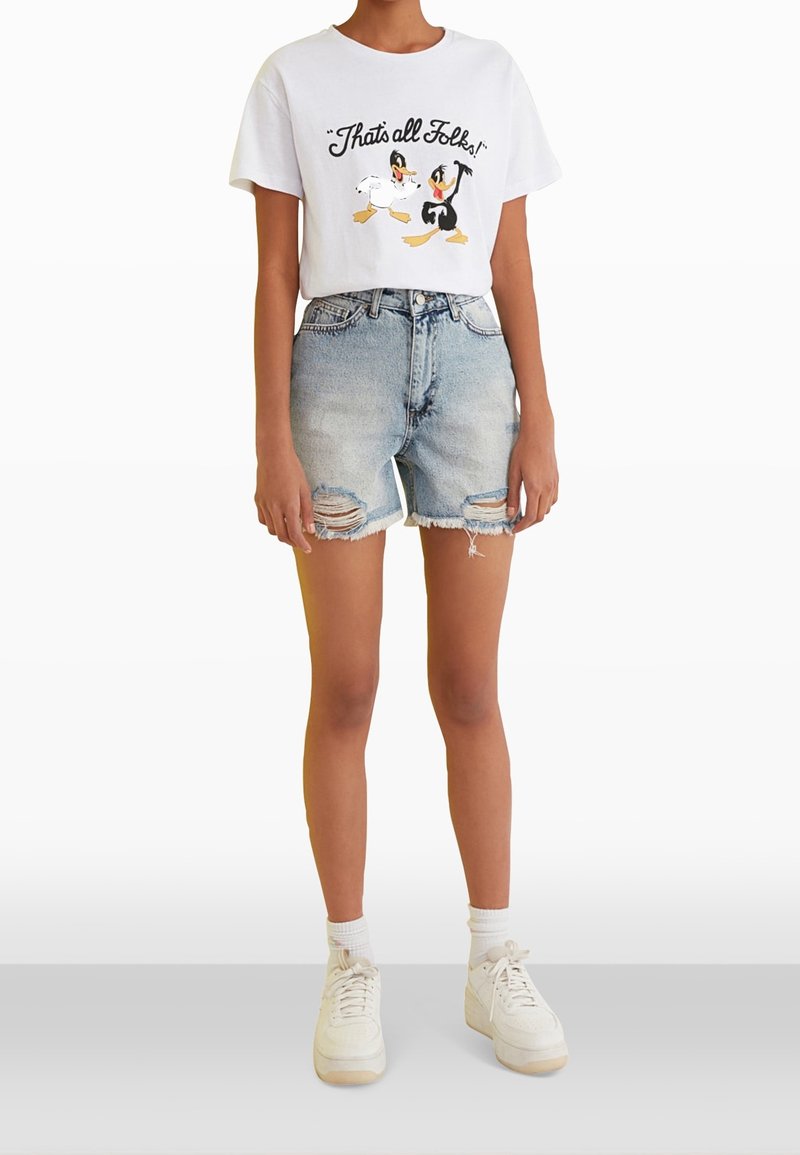 Camiseta blanca con personajes de dibujos animados y el texto "¡Eso es todo, amigos!" combinada con pantalones cortos de mezclilla desgastados en azul claro y zapatillas blancas.