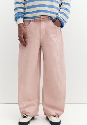 Person trägt hellrosa weit geschnittene Hosen mit Nahtdetails und Sneakers, kombiniert mit einem blau-weiß gestreiften Langarmshirt.