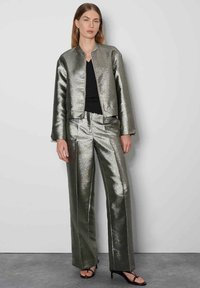Metallic zilveren bomberjack en bijpassende wijde broek, met een ritsluiting en contrasterende naden. Zwarte top en hakken.